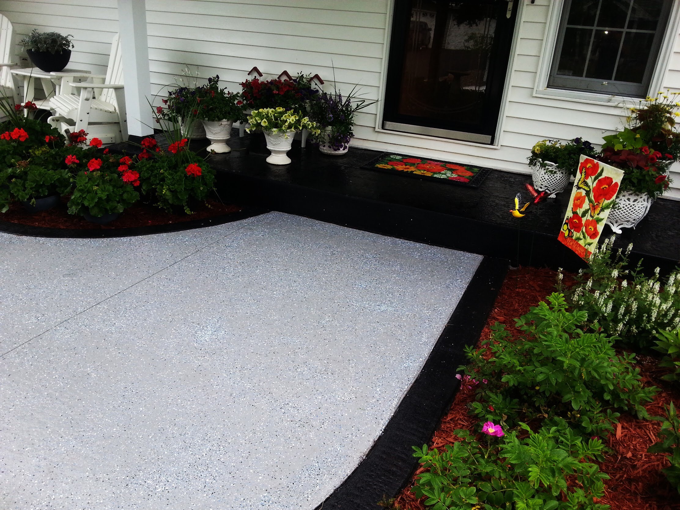 Flower-filled porch with potted plants, a freshly painted gray walkway, and decorative elements, showcasing a vibrant, welcoming outdoor space.
