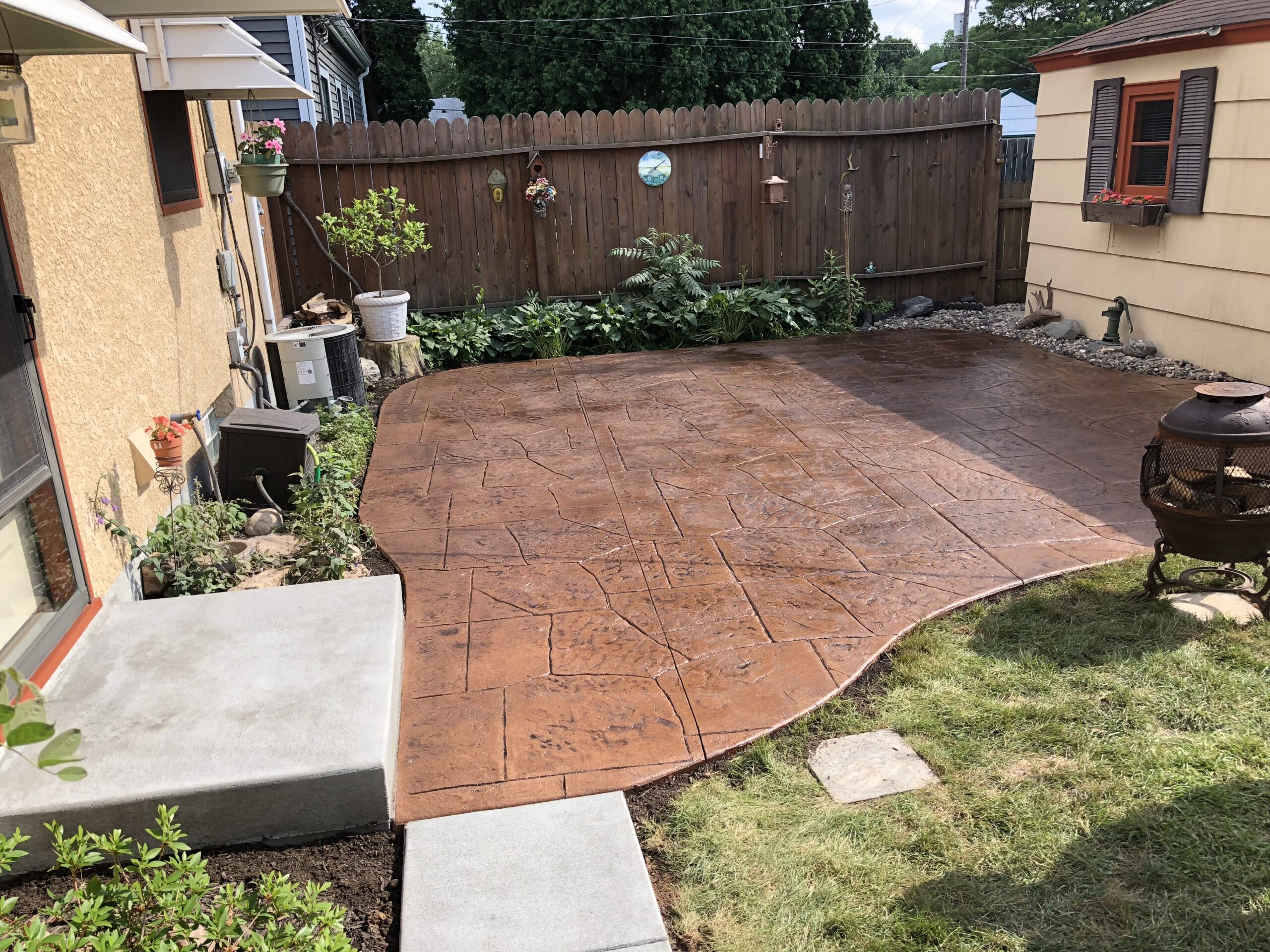 Newly laid stamped concrete patio in a backyard, surrounded by plants and garden decor, providing an inviting outdoor space.