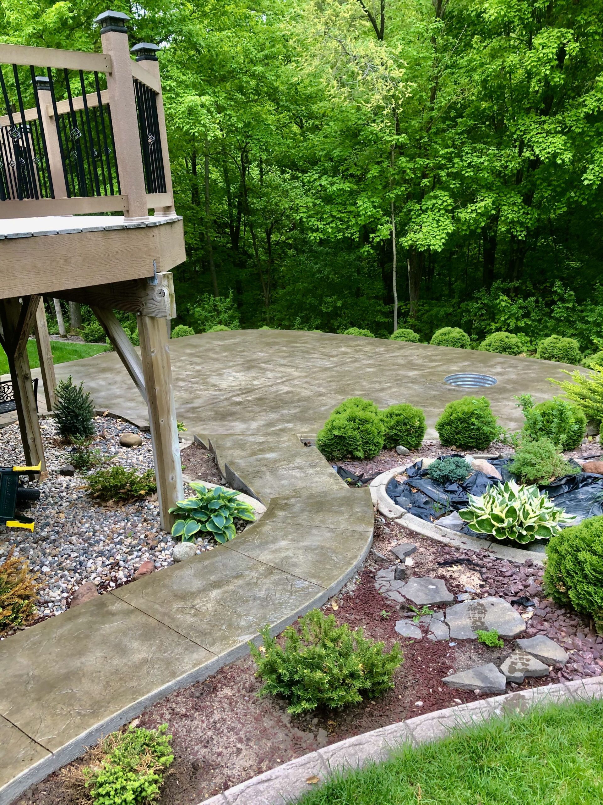 Backyard patio showcasing a textured concrete surface surrounded by lush greenery and landscaped gardens, designed for outdoor relaxation.