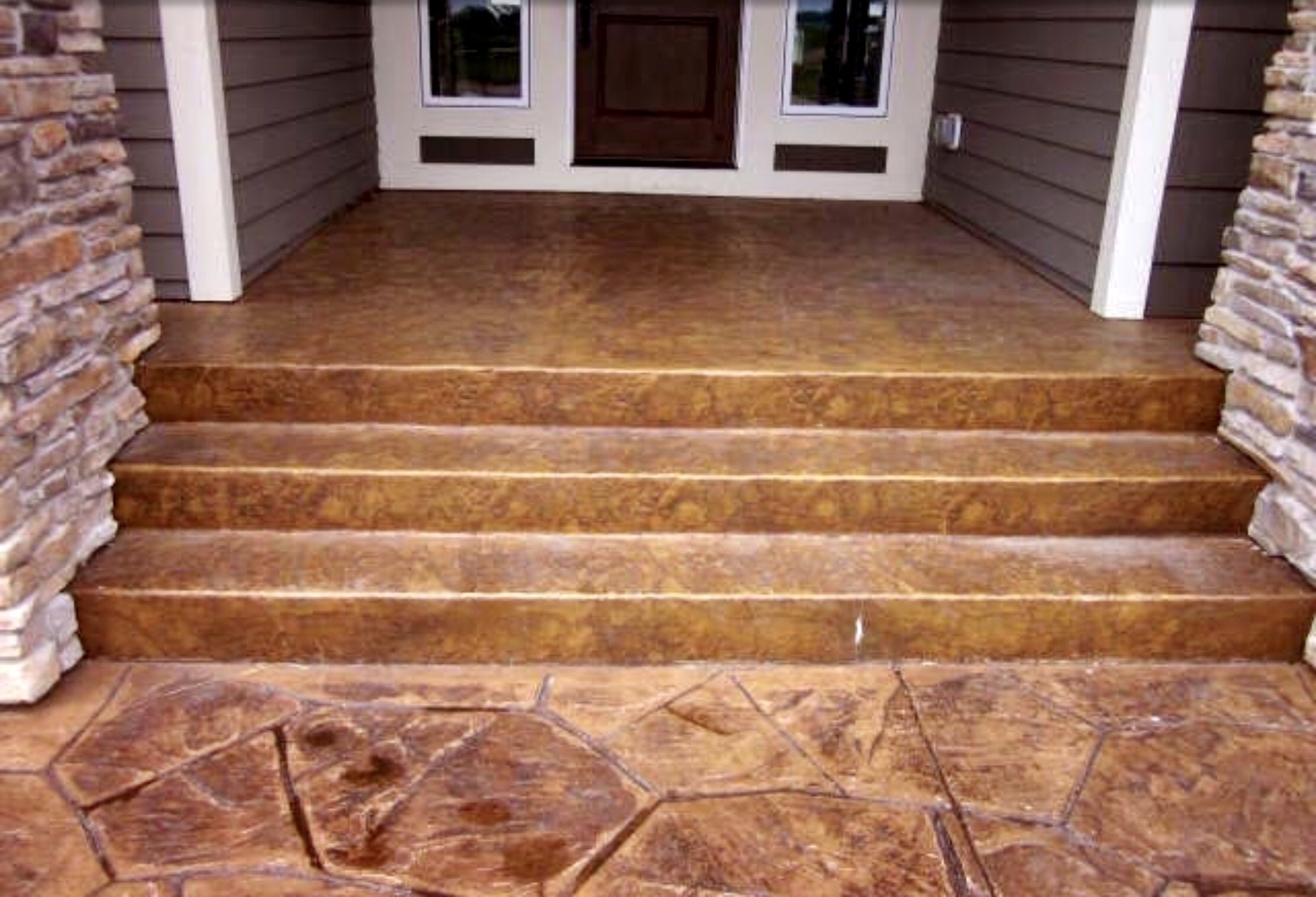 Decorative stamped concrete steps lead up to a front porch with stone accents, showcasing an inviting entryway for a home.